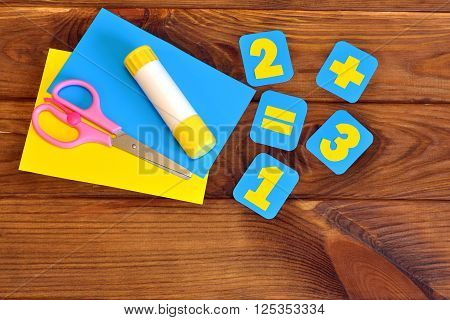 Handmade paper cards with numbers, scissors, paper sheets, glue on a brown wooden background
