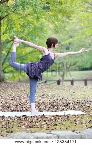 Japanese woman outside doing yog Lord of the Dance Pose