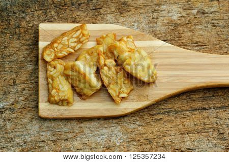 Fried Tempeh in wooden spatula on textured background. Tempeh is made from soy bean and popular in some part of Asia.