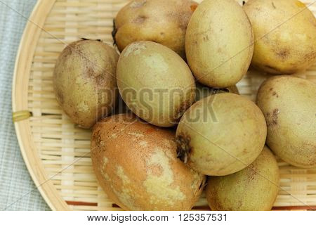 Raw Sapodilla in rattan tray on textured background