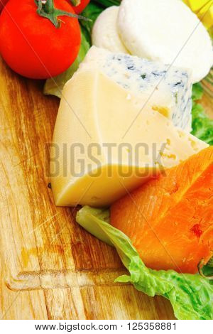 fresh aged french cheeses chops on big cutting board with tomatoes olive oil, rye breadm and green chives isolated over white background