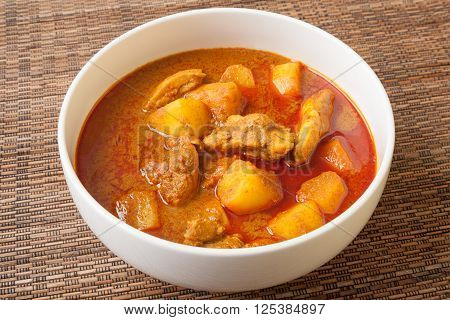 Spicy Thai red chicken curry called Massaman curry in white bowl sitting on bamboo mat