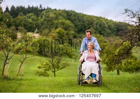 Senior man pushing woman sitting in wheelchair oustide in green autumn nature
