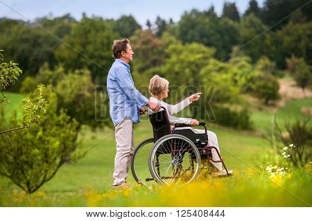 Senior man pushing woman sitting in wheelchair oustide in green autumn nature