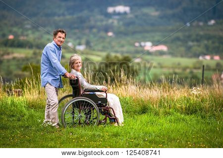 Senior man pushing woman sitting in wheelchair oustide in green autumn nature