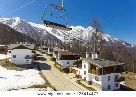 ROSA KHUTOR, RUSSIA - APRIL 01, 2016: Mountain ski resort Rosa Khutor with cottages on snowy mountains background