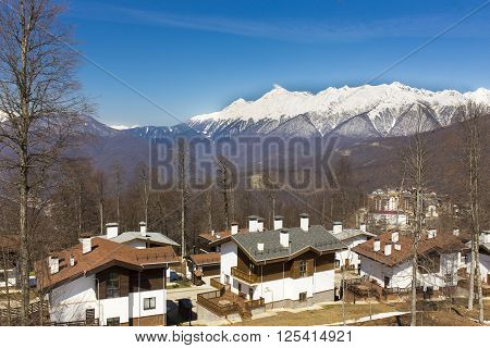 ROSA KHUTOR, RUSSIA - APRIL 01, 2016: Mountain ski resort Rosa Khutor with cottages on snowy mountains background