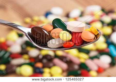 Colorful medical pills on teaspoon and capsules or supplements for therapy in background concept of treatment and health care