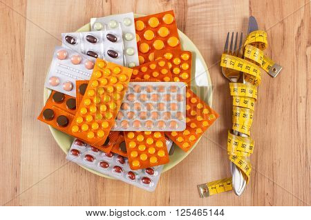Fork and knife wrapped tape measure and blisters of medical pills capsules or supplements for therapy on plate concept of treatment health care slimming