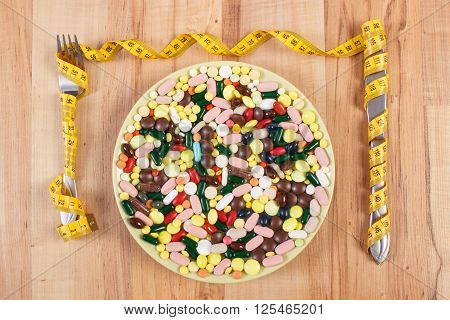 Fork and knife wrapped tape measure and medical pills capsules or supplements for therapy on plate concept of treatment health care slimming