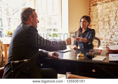 Woman passing room key to a guest at check-in desk of hotel