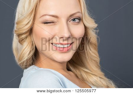 Give me a wink. Cheerful charming young girl smiling and winking while expressing positivity