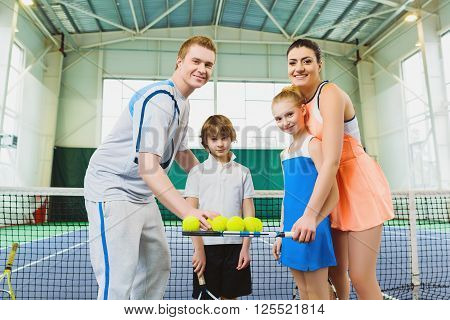 Young woman and man or coach teaching children how to play tennis on a court indoor.
