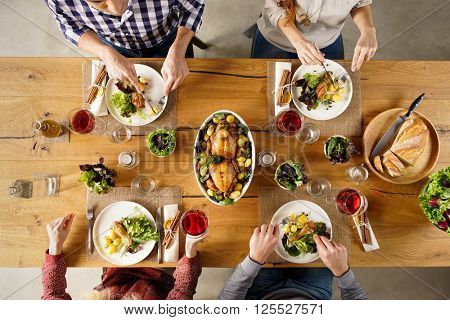 Top view of dining table with salad and roasted chicken with potatoes. High angle view of happy young friends having lunch at home. Men and women eating lunch together. 