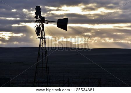 Landscape with water pump windmill at sunrise