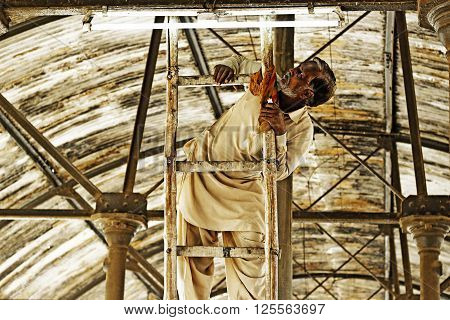 Hyderabad, Sindh Pakistan - November 11, 2014 - An old Electrician repairing tube light at railway station at  railway station as he is doing his routine job