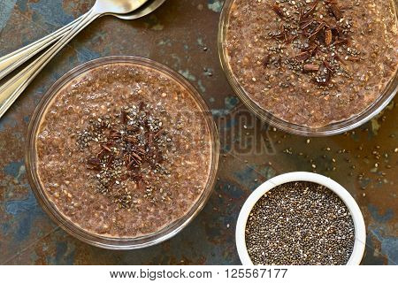 Chocolate chia seed pudding in glass bowls with chia seeds and chocolate shavings on top photographed overhead on slate with natural light