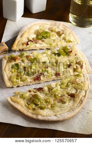 Homemade leek and bacon tarte flambee a traditional French and German oven baked pizza-like pie photographed on parchment paper with natural light (Selective Focus Focus on the front of the middle slice)
