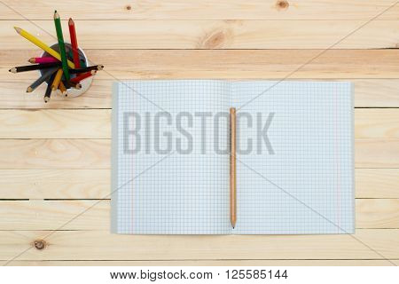 Open notebook with colored pencils on the wooden table.