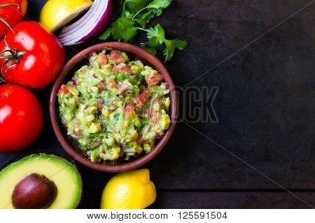 Guacamole - latin american mexican sauce in stone mortar and ingredients on dark background. Top view