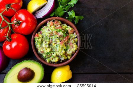 Guacamole - latin american mexican sauce in stone mortar and ingredients on dark background. Top view