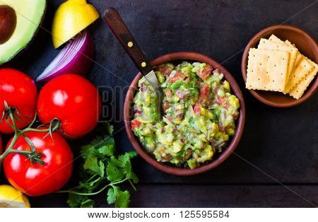 Guacamole - latin american mexican sauce in stone mortar and ingredients on dark background. Top view