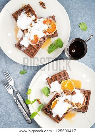 Belgian soft waffles with blood orange, cream, marple syrup and mint  on white plates over concrete textured background. Top view