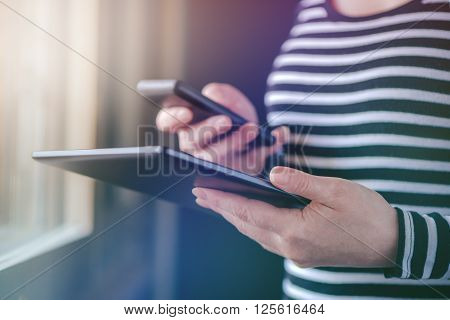 Smartphone and tablet data synchronization woman syncing files and documents on personal wireless electronic devices at home selective focus with shallow depth of field.