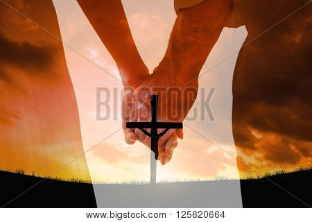Bride and groom holding hands close up against cross religion symbol shape over sunset sky