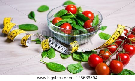 Diet Concept - Salad With Spinach And Tomatoes And Measure Tape On Wooden Table