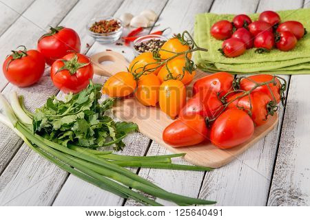 close up of fresh red and yellow delicious tomatoes with greenery on an old wooden background