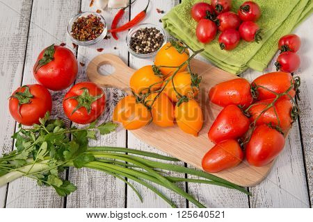close up of fresh red and yellow delicious tomatoes with greenery on an old wooden background