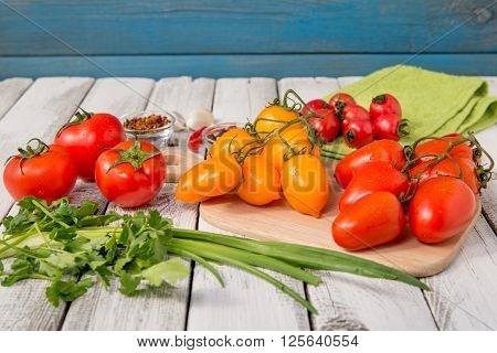 close up of fresh red and yellow delicious tomatoes with greenery on an old wooden background