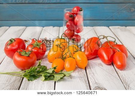 close up of fresh red and yellow delicious tomatoes with greenery on an old wooden background
