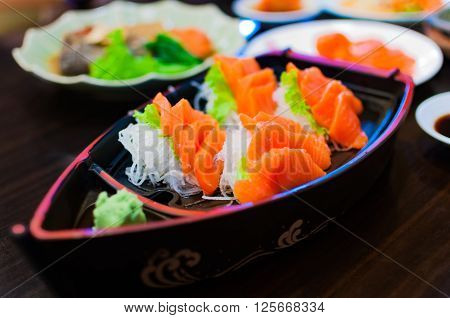 Selective focus of raw fresh sashimi serve in a boat bowl with green wasabi and sliced radish