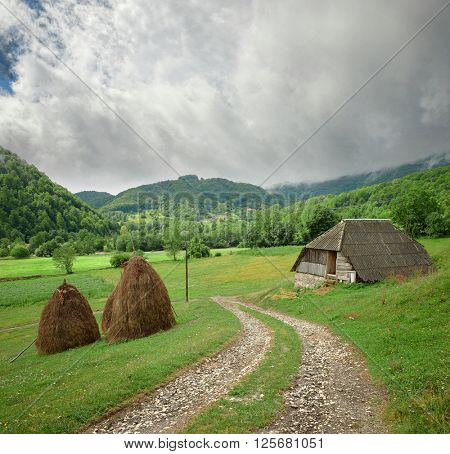 path crosses rural landscape with haystacks in Montenegro Mountains
