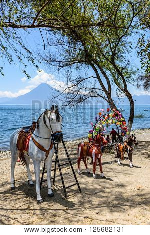 Lake Atitlan Guatemala - April 4 2016: Local families relax on shores of Lake Atitlan with San Pedro volcano behind. Parents pay for children to sit on life size model horses.