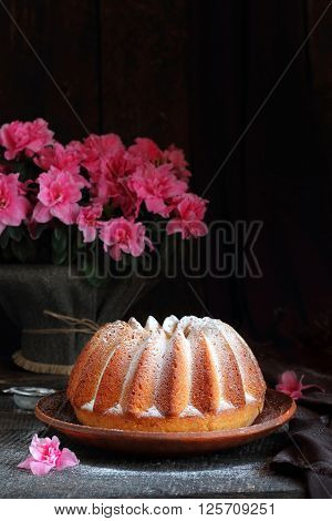 orange cake sprinkled with powdered sugar and azalea flowers on a dark background
