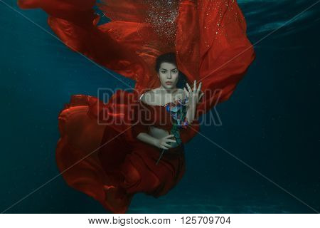 Woman in a red dress under water in the hands holding flowers.