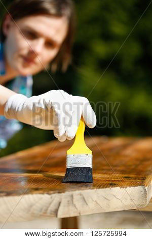 Woman carpenter inspecting her work after treating wood with protection paint. Outdoor protection carpentry hard at work quality control home improvement do-it-yourself concept.