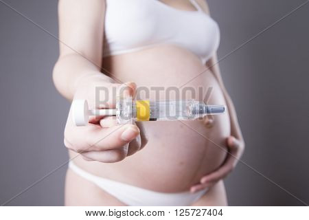 Young pregnant woman making injection in the stomach. Close-up studio shot on a gray background
