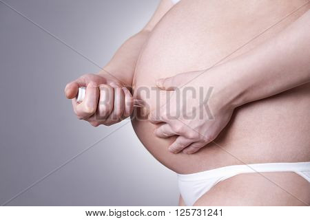 Young pregnant woman making injection in the stomach. Close-up studio shot on a gray background