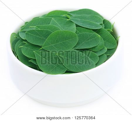 Moringa leaves in a bowl over white background