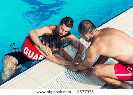Lifeguards with victim on poolside with drowner
