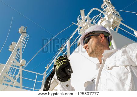 Deck officer speaking by VHF on radar deck under blue sky