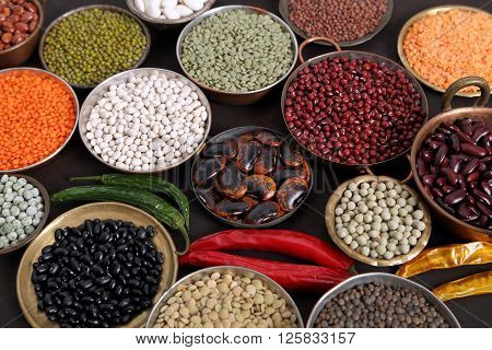 Beans peas and lentils in metal bowls on dark background.