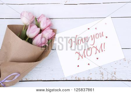 Beautiful bouquet of pink tulips next to a white envelope and pink sugar hearts on light wooden background