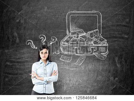 Businesswoman with hands crossed open case with money drawn on black wall behind question marks over her head. Concept of making money.