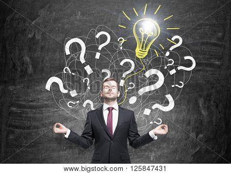 Idea concept with businessman meditating against wall with question mark and bulb sketch
