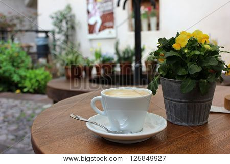 Cup of cappuccino with pansies in a pot on the table. White cup of coffee with spoon on the table outside terrace. Yellow pansies pot aside. Small Italian terrace and patio.
** Note: Visible grain at 100%, best at smaller sizes